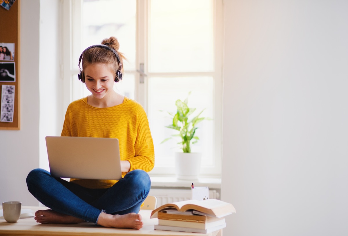 A student sitting cross-legged with a laptop in a bright room
